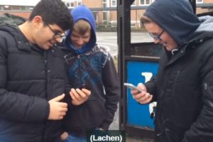 Drei Jugendliche schauen auf ihre Handys und lachen höhnisch