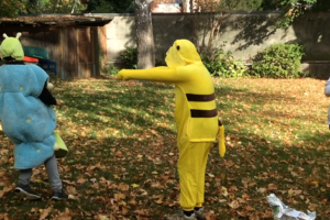 Ein Jugendlicher als Pikachu verkleidet, verfolgt einen anderen als Raupe verkleidet. Ein dritter schaut schockiert zu.
