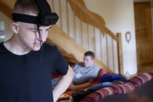 Ein Jugendlicher mit GoPro-Kopfhalterung im Vordergrund. Im Hintergrund ein weiterer Jugendlicher auf einem Sofa.