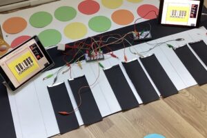 Auf dem Boden liegt ein Klavier aus Stoff. Es ist an bunte Kabel angeschlossen. Daneben stehen Tablets.