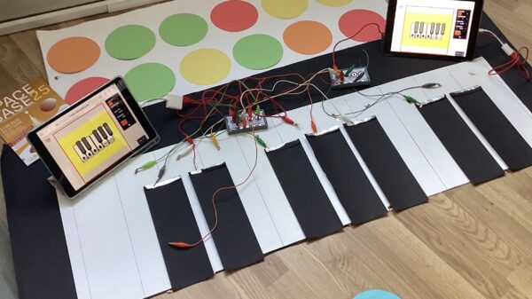 Auf dem Boden liegt ein Klavier aus Stoff. Es ist an bunte Kabel angeschlossen. Daneben stehen Tablets.