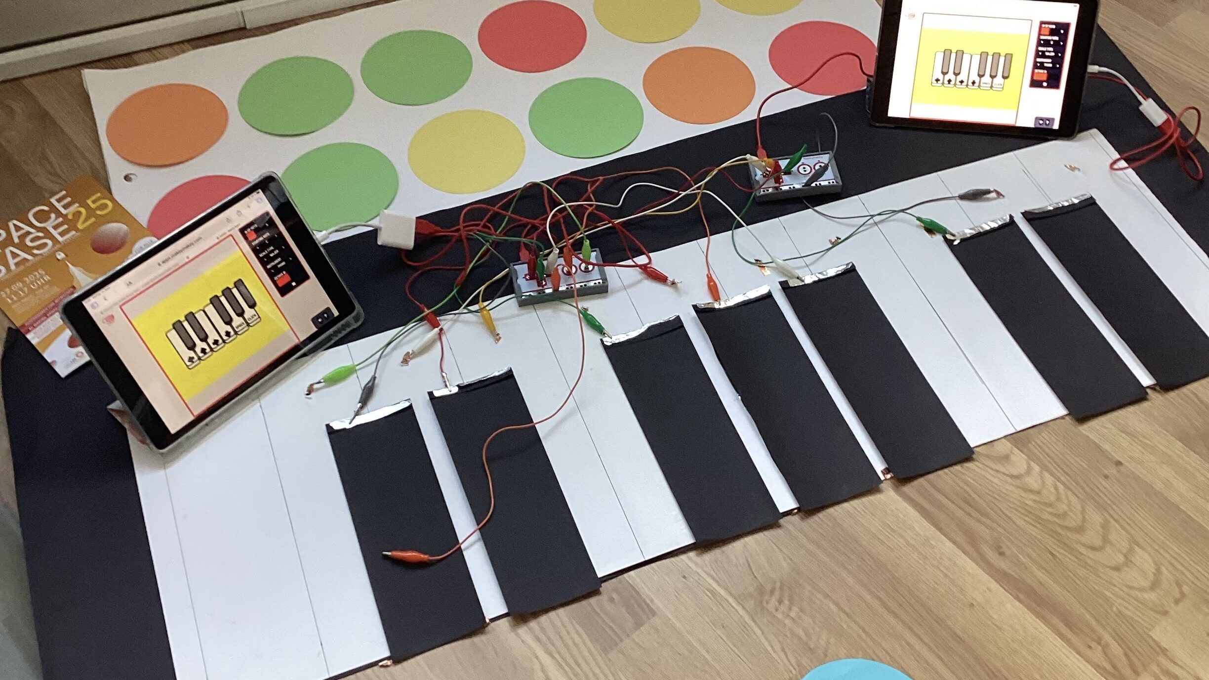 Auf dem Boden liegt ein Klavier aus Stoff. Es ist an bunte Kabel angeschlossen. Daneben stehen Tablets.