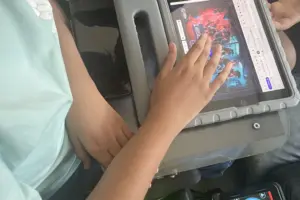Kind im Rollstuhl bedient mit der rechten Hand ein Tablet mit Escape-Room-Spiel, das auf einem Rollstuhl-Tablett befestigt ist.